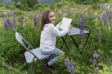 Smiling girl with book amidst lupine flowers in meadow - OSF00753