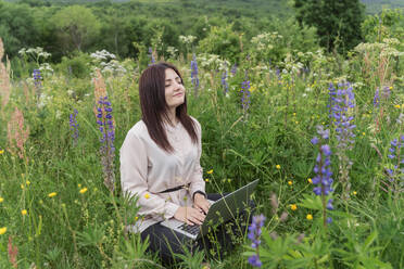 Freelancer with laptop and eyes closed sitting in meadow - OSF00765