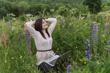 Freelancer with laptop relaxing amidst flowers in meadow - OSF00766