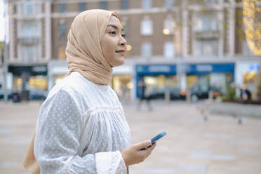 Nachdenkliche Frau mit Smartphone auf der Straße - AMWF00301