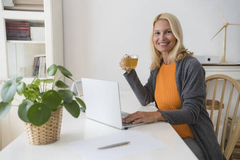 Lächelnde Freiberuflerin mit Teetasse am Schreibtisch im Home Office - SVKF00497