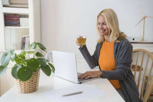 Glücklicher Freiberufler mit Teetasse bei der Arbeit am Laptop im Home Office - SVKF00498