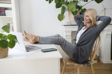 Smiling freelancer with hands behind hand sitting on chair in home office - SVKF00509