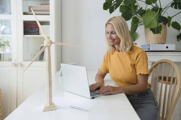 Smiling freelancer with blond hair working on laptop at desk in home office - SVKF00510