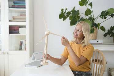 Lächelnder Freiberufler mit Windradmodell am Schreibtisch im Home Office - SVKF00512