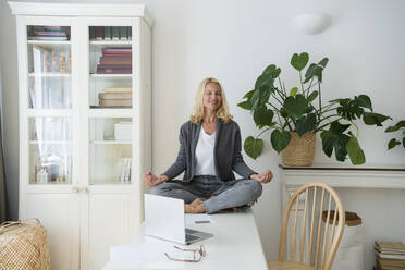 Lächelnder Freiberufler mit geschlossenen Augen beim Meditieren auf dem Schreibtisch im Heimbüro - SVKF00517
