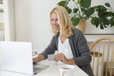 Smiling woman holding credit card using laptop at home - SVKF00519