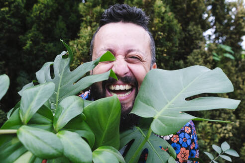 Cheerful man with plant at back yard - ASGF02697