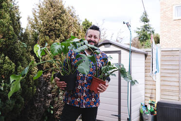 Lächelnder Mann mit Topfpflanzen im Hinterhof stehend - ASGF02698