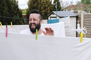 Fröhlicher Mann trocknet Laken auf einer Wäscheleine im Hinterhof - ASGF02701