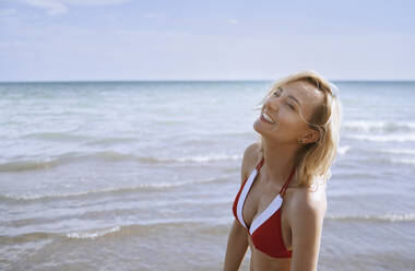 Lächelnde Frau genießt das Sonnenlicht am Strand - AZF00417
