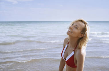 Smiling woman enjoying sunlight at beach - AZF00417