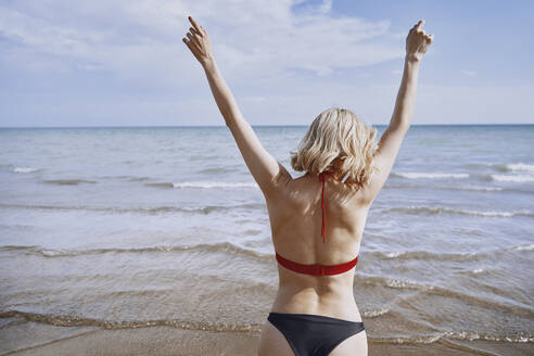 Frau mit erhobenen Armen genießt am Strand an einem sonnigen Tag - AZF00421