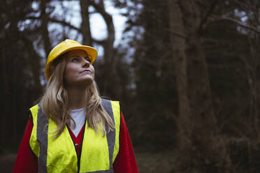 Thoughtful worker in reflective clothing standing in forest - AMWF00307