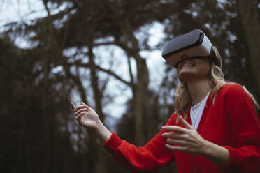 Woman in red sweater wearing virtual reality simulator in forest - AMWF00308