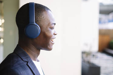 Glücklicher junger Mann mit kabellosen Kopfhörern beim Musikhören - AMWF00338