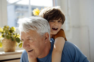 Happy senior man giving piggyback ride to grandson at home - JOSEF12080