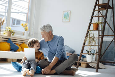 Boy holding tablet PC talking with grandfather in living room - JOSEF12081