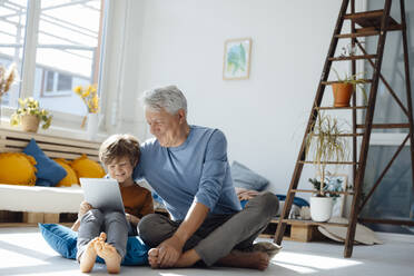 Smiling boy using tablet PC by grandfather in living room - JOSEF12084