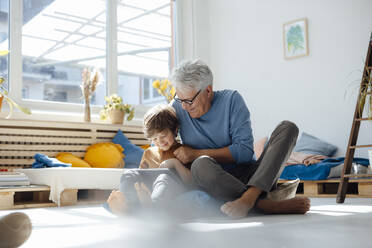 Smiling grandson using tablet PC by grandfather at home - JOSEF12085