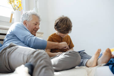 Smiling grandfather pointing at tablet PC by grandson in living room - JOSEF12086