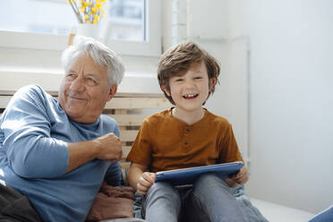 Happy boy with tablet PC sitting by grandfather at home - JOSEF12087