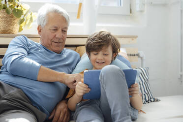 Smiling boy sharing tablet PC with grandfather at home - JOSEF12089