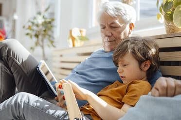 Grandfather looking at grandson with abacus sitting on sofa - JOSEF12090