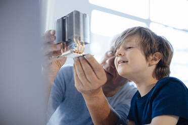 Grandfather examining model object by grandson at home - JOSEF12096