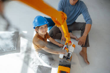 Smiling boy playing with crane toy by grandfather at home - JOSEF12105