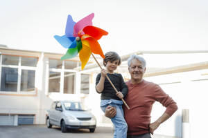 Smiling grandfather carrying grandson with pinwheel toy - JOSEF12108