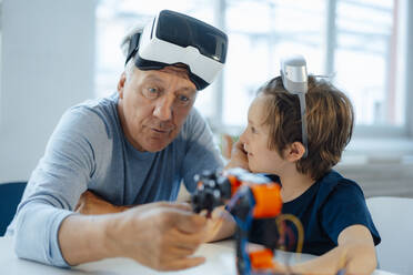 Senior man with VR glasses examining robot model by grandson at home - JOSEF12112