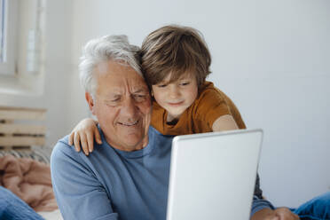 Smiling senior man taking selfie with grandson through tablet PC at home - JOSEF12113