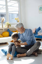 Smiling senior man using tablet PC with grandson in living room - JOSEF12117