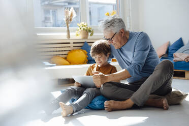 Senior man using tablet PC with grandson in living room - JOSEF12118