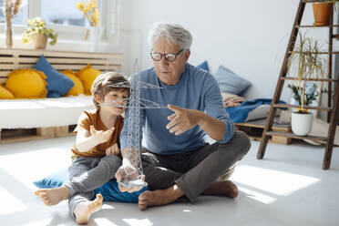 Grandson and grandfather examining electricity pylon model in living room - JOSEF12121