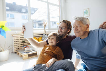 Lächelnder Mann, der ein Selfie mit Sohn und Vater über einen Tablet-PC zu Hause macht - JOSEF12129