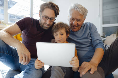 Junge schaut mit Vater und Großvater einen Film auf einem Tablet-PC zu Hause - JOSEF12133