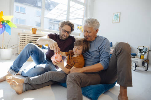 Senior man with son and grandson putting money in piggy bank at home - JOSEF12134