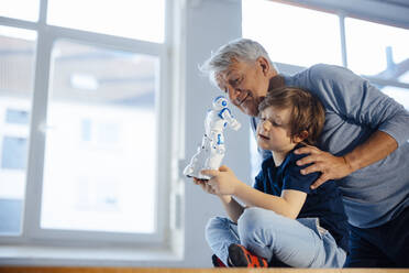 Smiling senior man by grandson with robot model at home - JOSEF12159