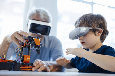 Senior man and boy with VR glasses watching robot model at home - JOSEF12161