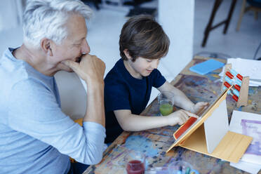 Smiling boy using tablet PC by grandfather at home - JOSEF12170