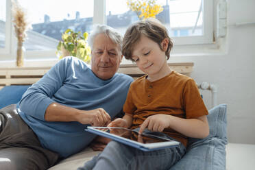 Boy using tablet PC by grandfather in living room - JOSEF12176