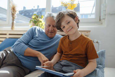 Smiling boy with tablet PC by grandfather at home - JOSEF12177