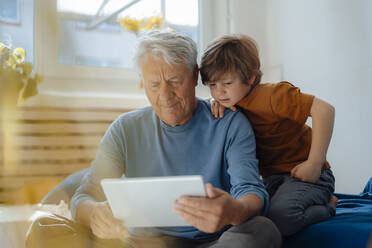 Senior man sharing tablet PC with grandson in living room at home - JOSEF12190