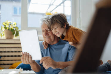 Happy senior man taking selfie with grandson through tablet PC at home - JOSEF12193