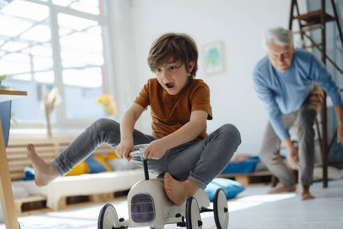 Happy boy on toy car playing with grandfather at home - JOSEF12199