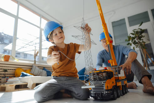 Junge imitiert einen Ingenieur, der ein Modell eines Strommastes untersucht, mit seinem Großvater im Hintergrund zu Hause - JOSEF12205
