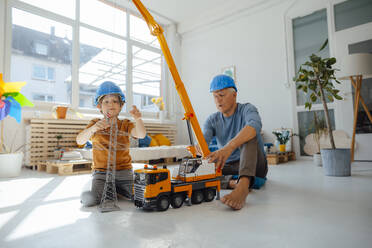 Junge imitiert Ingenieur, der mit seinem Großvater zu Hause ein Modell eines Strommastes an einem Spielzeugkran befestigt - JOSEF12207