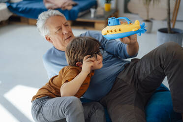 Grandfather and grandson examining submarine toy at home - JOSEF12208